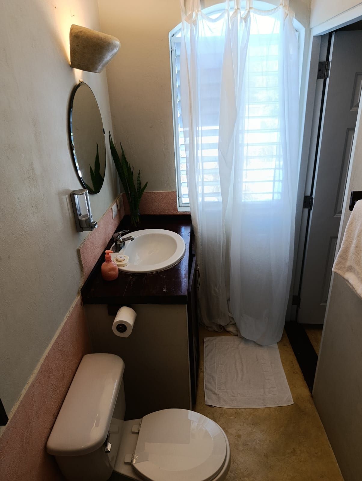 Small bathroom with a toilet, sink, and shower. Pink and beige walls, white shower curtain.