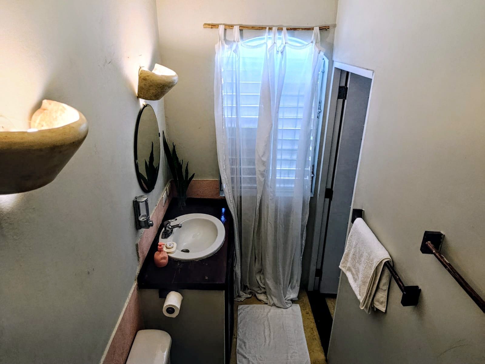 Small bathroom with sink, toilet, window with curtains, towel rack.