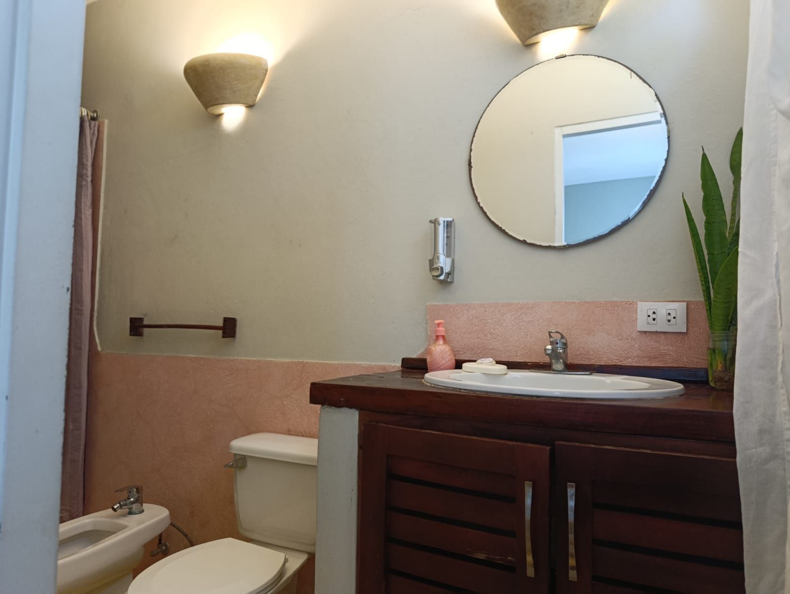 Bathroom with a round mirror, wooden vanity, and pink accents.