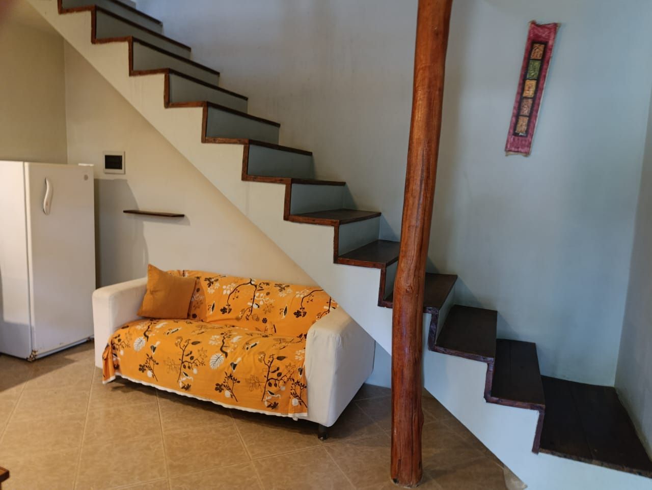 White sofa under wooden stairs; fridge on the left.