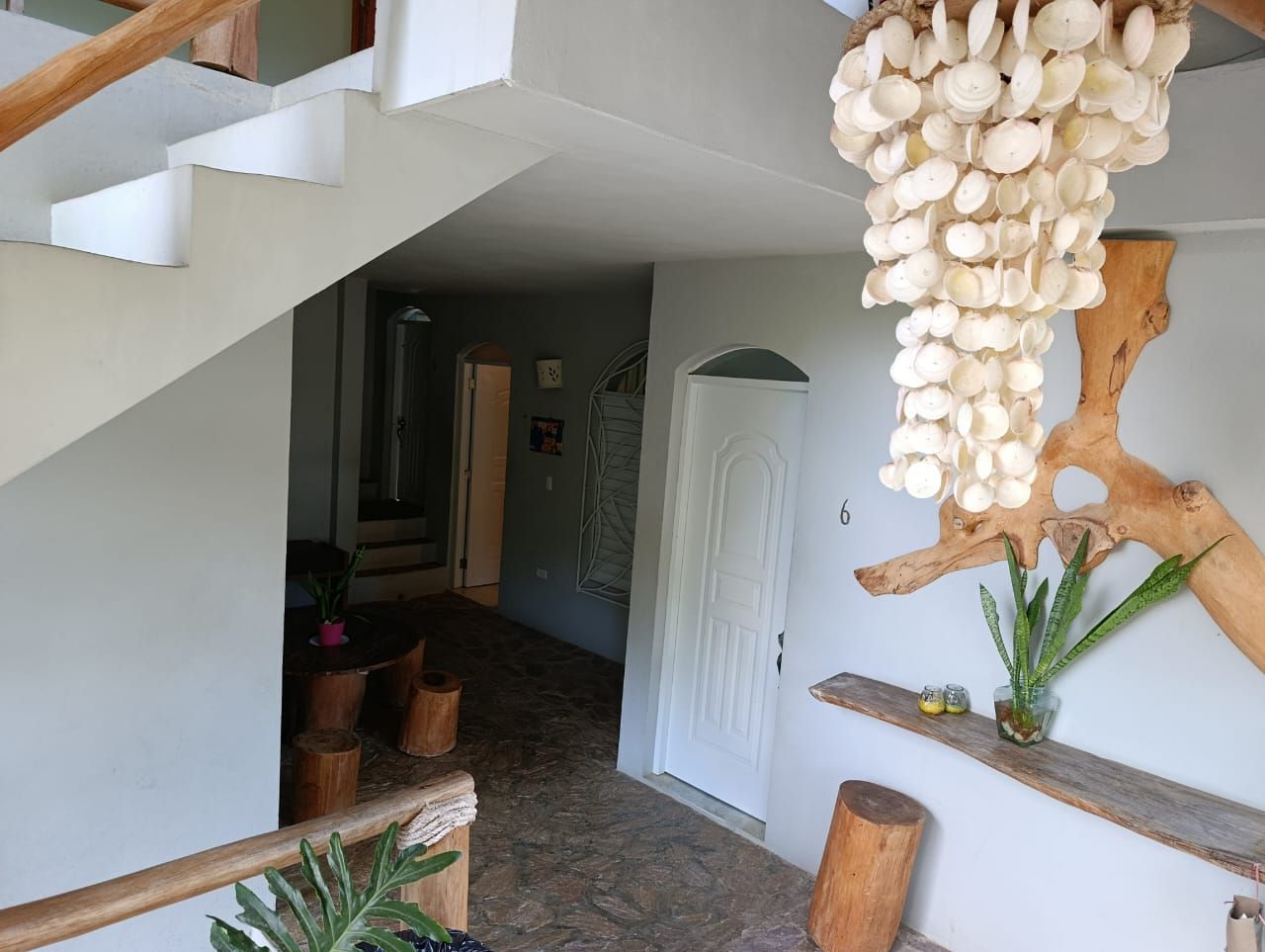 Staircase and hallway with a shell chandelier, wood accents, and a door, in a home.