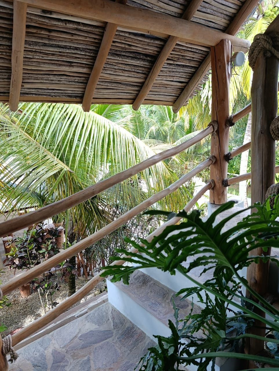 Wooden railing with a view of greenery, stairs, and a thatched roof.