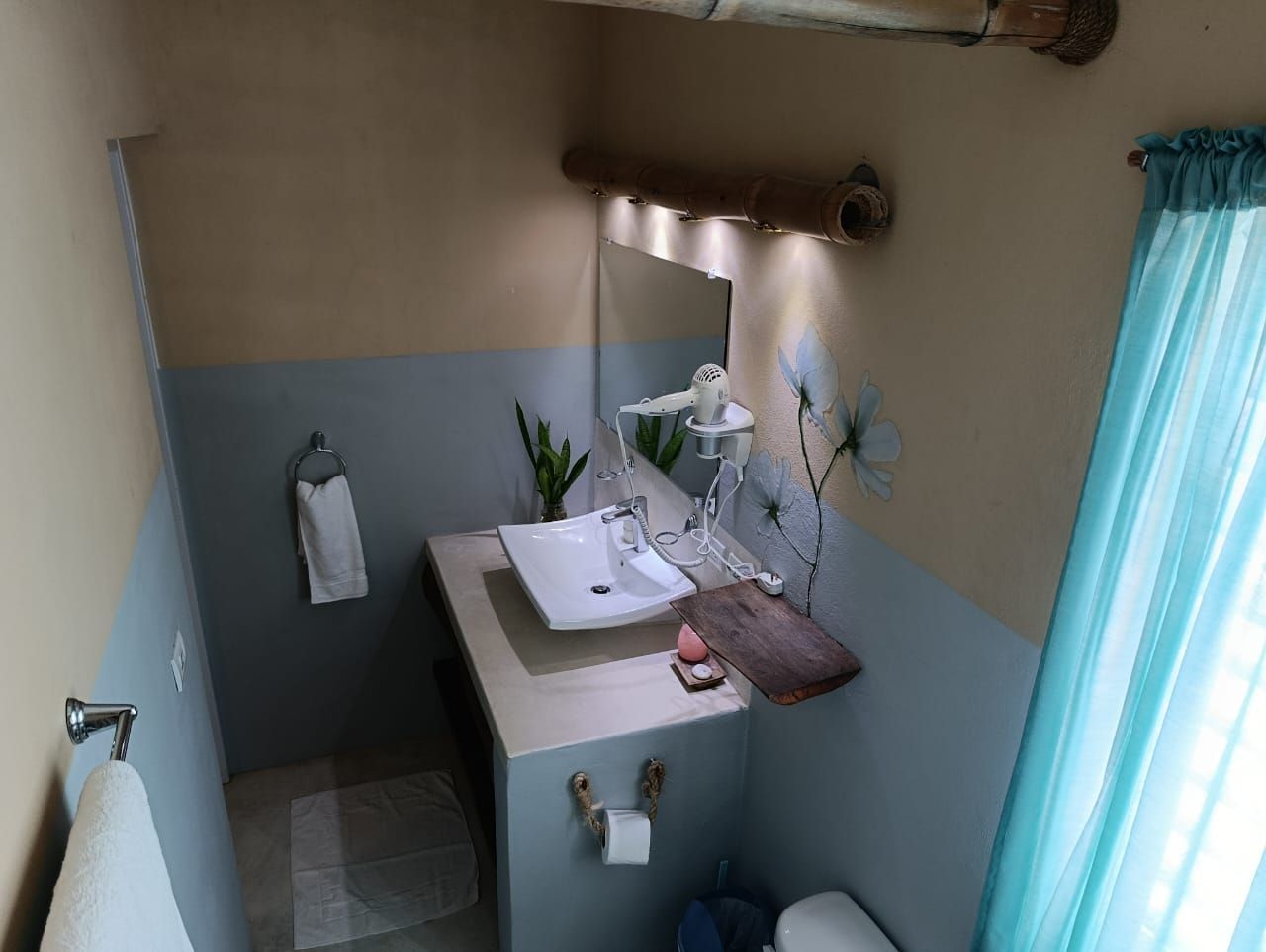 Small bathroom with white sink, blue and beige walls, wood accents, and sheer blue curtain.
