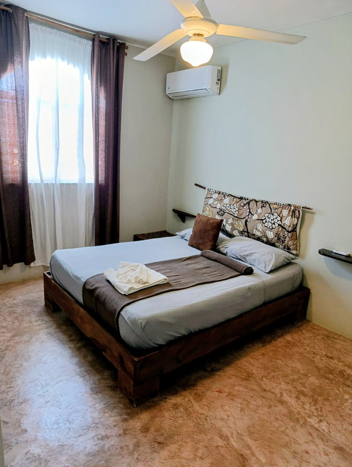 Bedroom with a wooden bed, gray bedding, floral headboard, brown curtains, and a ceiling fan.