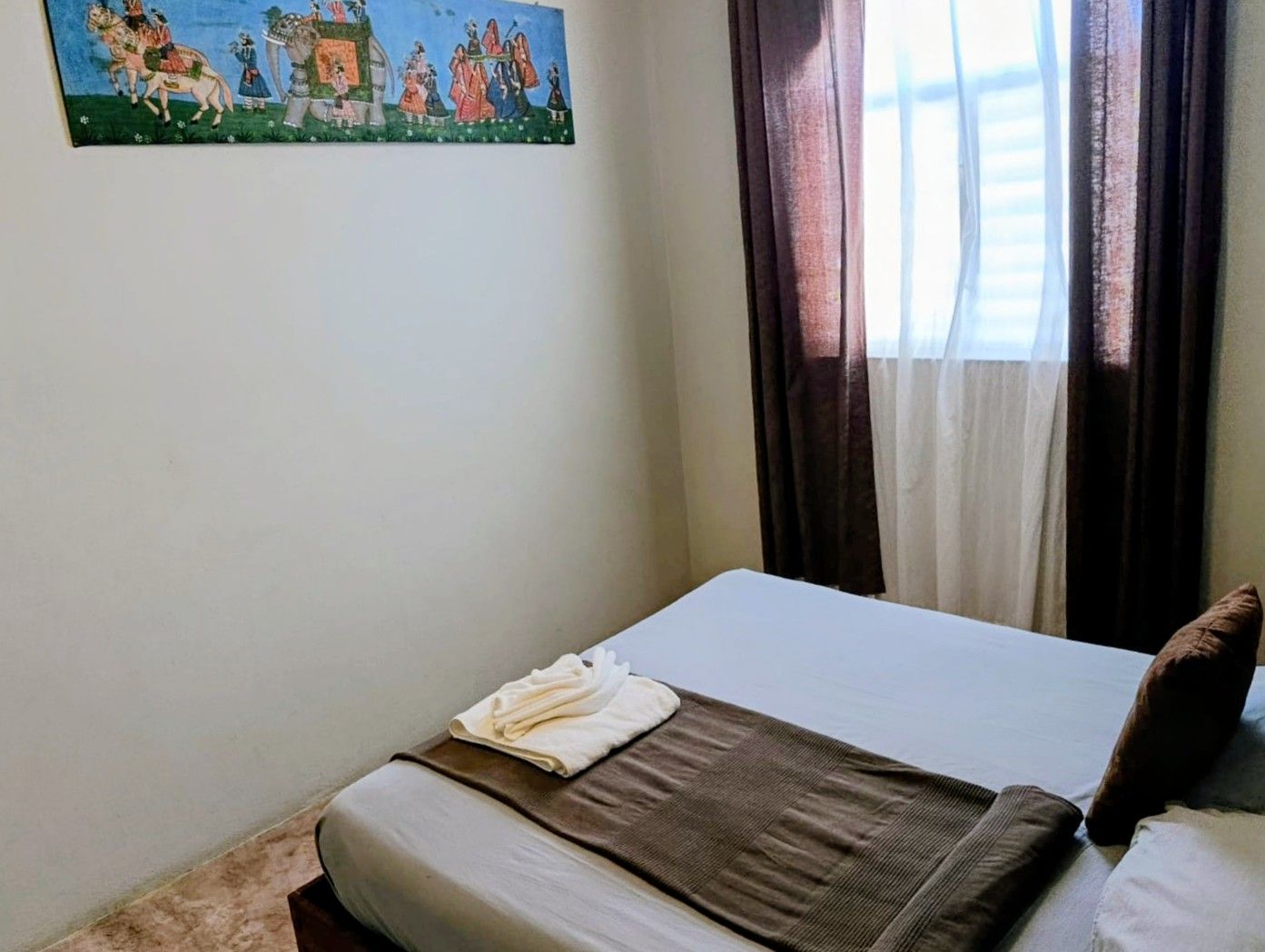 Bedroom with bed, brown drapes, artwork above, and white towels on the bed.