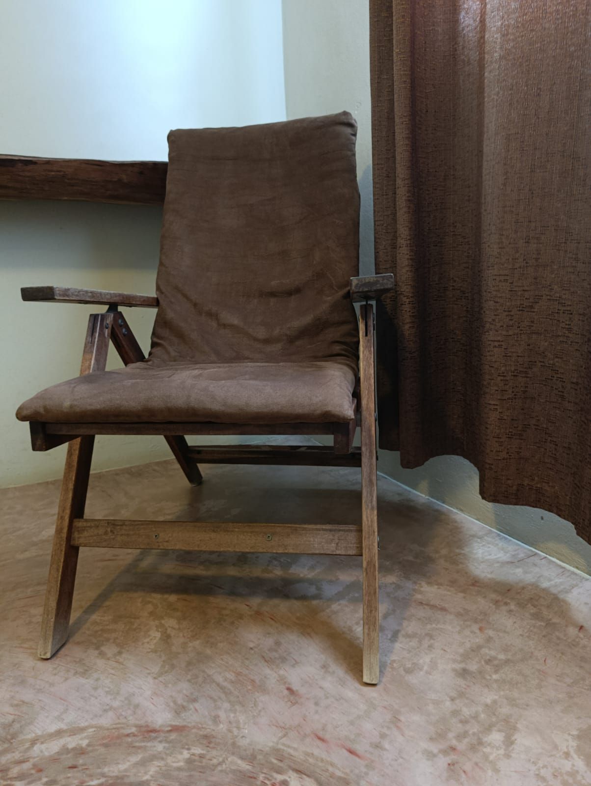 Brown wooden armchair with a cushion, near a brown curtain.