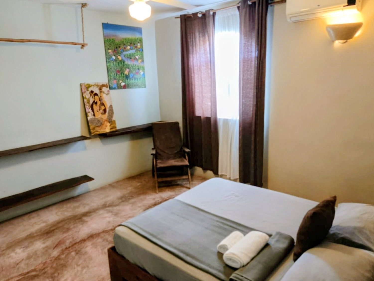 Bedroom with bed, chair, artwork, brown curtains, and a fluffy, pinkish rug.