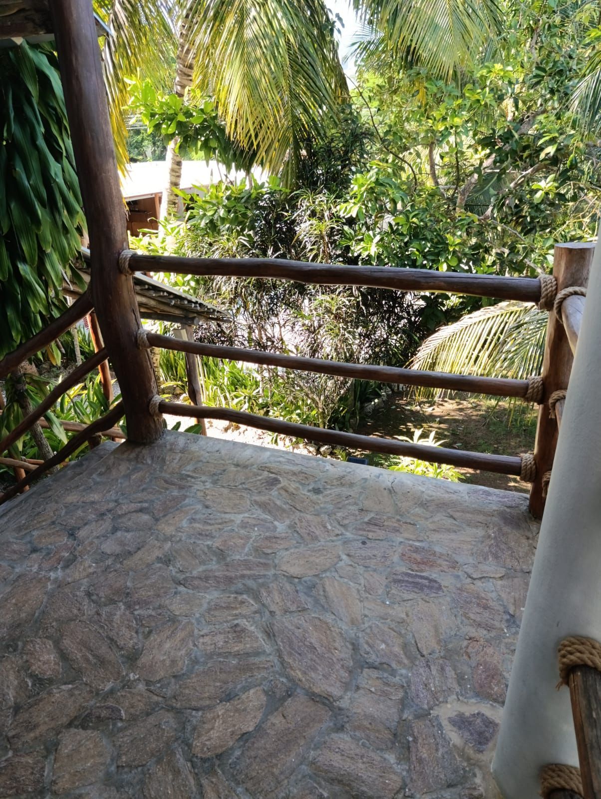 Balcony with stone floor, wooden railing, overlooking lush green foliage.