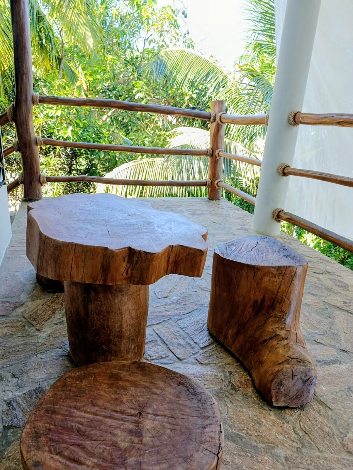 Wooden table and stools on a balcony with a natural setting in the background.