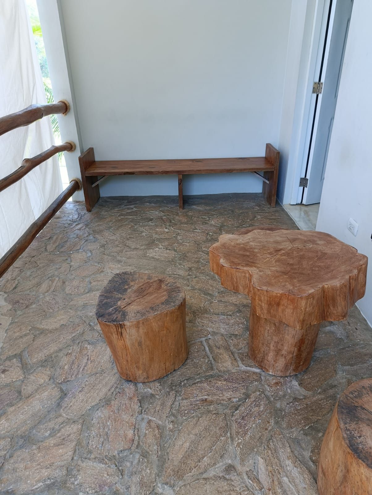 Rustic outdoor seating area with stone floor, wooden bench, and tree stump tables.