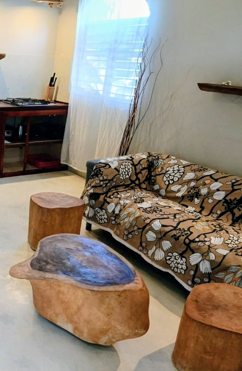 Living room with floral sofa, tree stump tables, and window with sheer curtain.