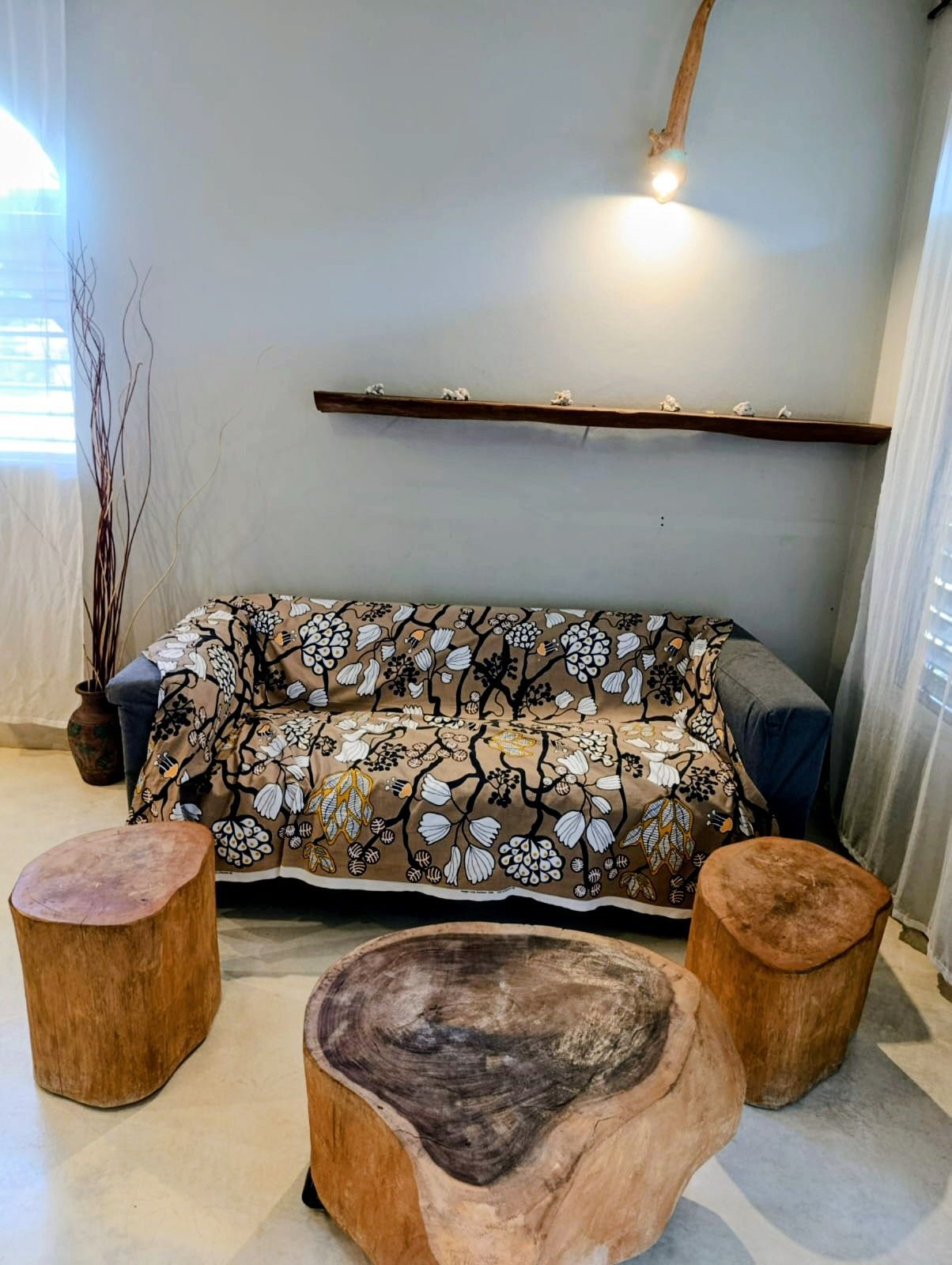 Living room: sofa with floral cover, three wood stump tables, shelf with candles, and a hanging light.