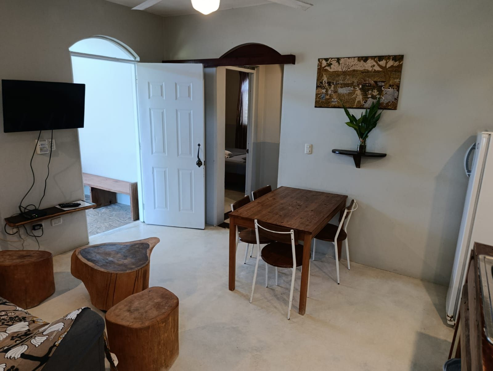 A living space with a dining area. Features a table with chairs, a TV, and a door leading to a bedroom.