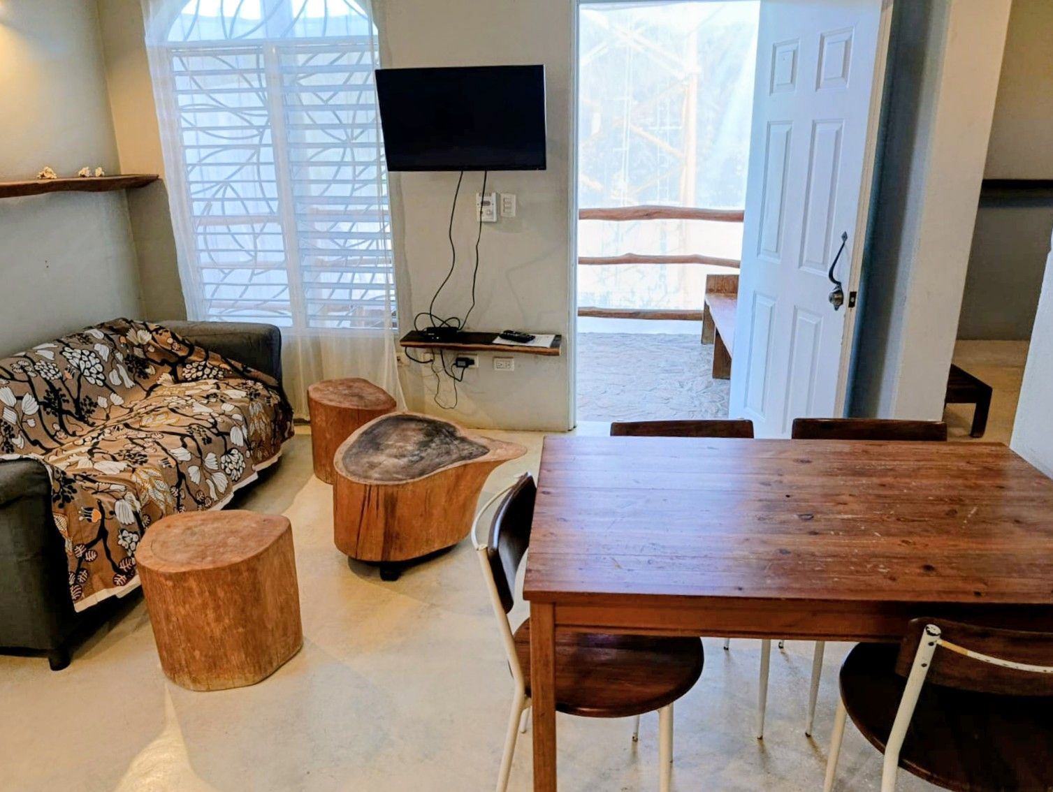 Cozy living area with sofa, wooden stools, table, TV, and open doorway to balcony.