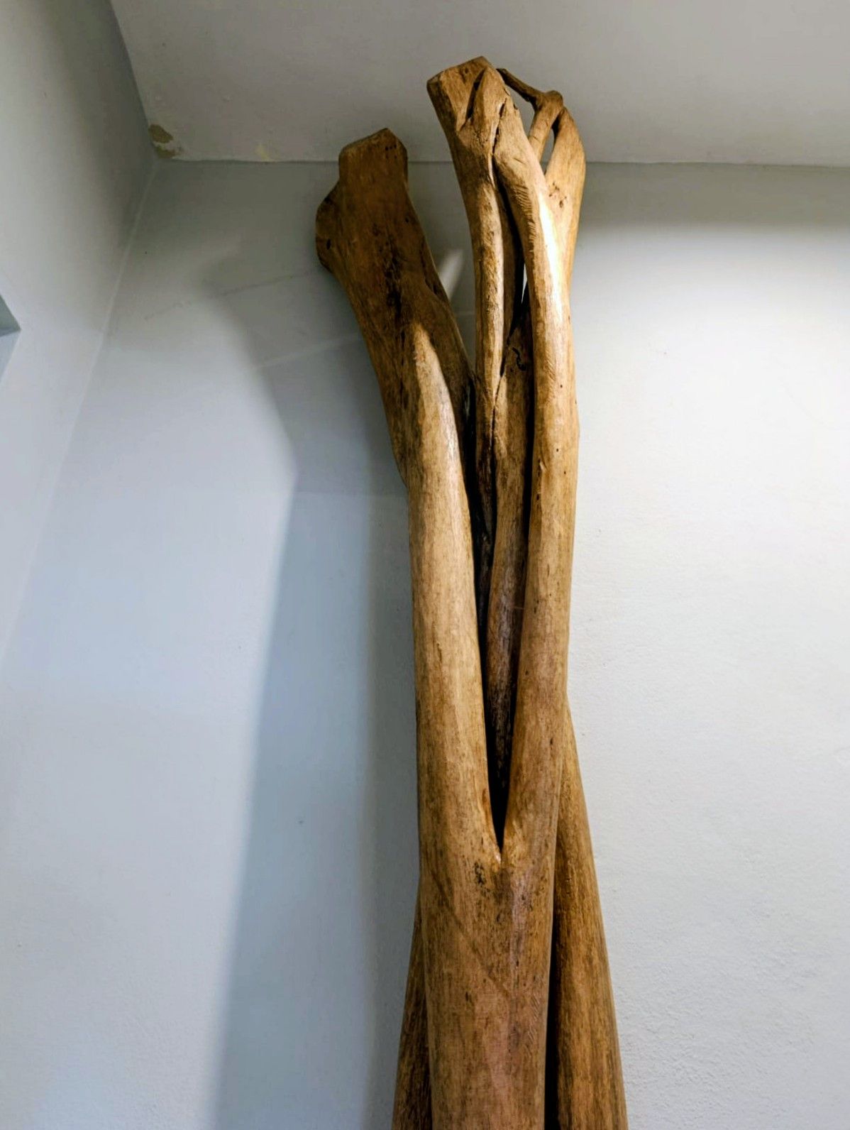 Tall, weathered wooden sculpture leaning against a light blue wall.