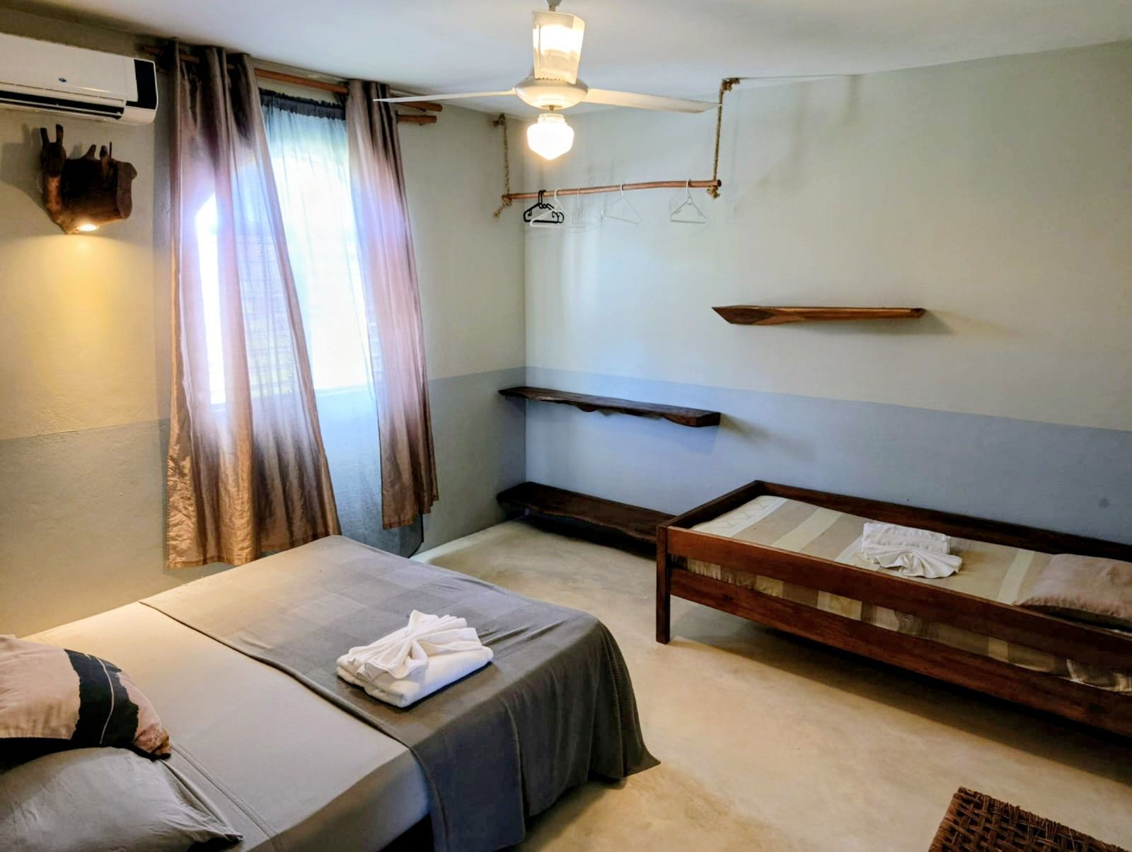 Bedroom with two beds, window, and shelves. Gray and brown tones, simple décor.