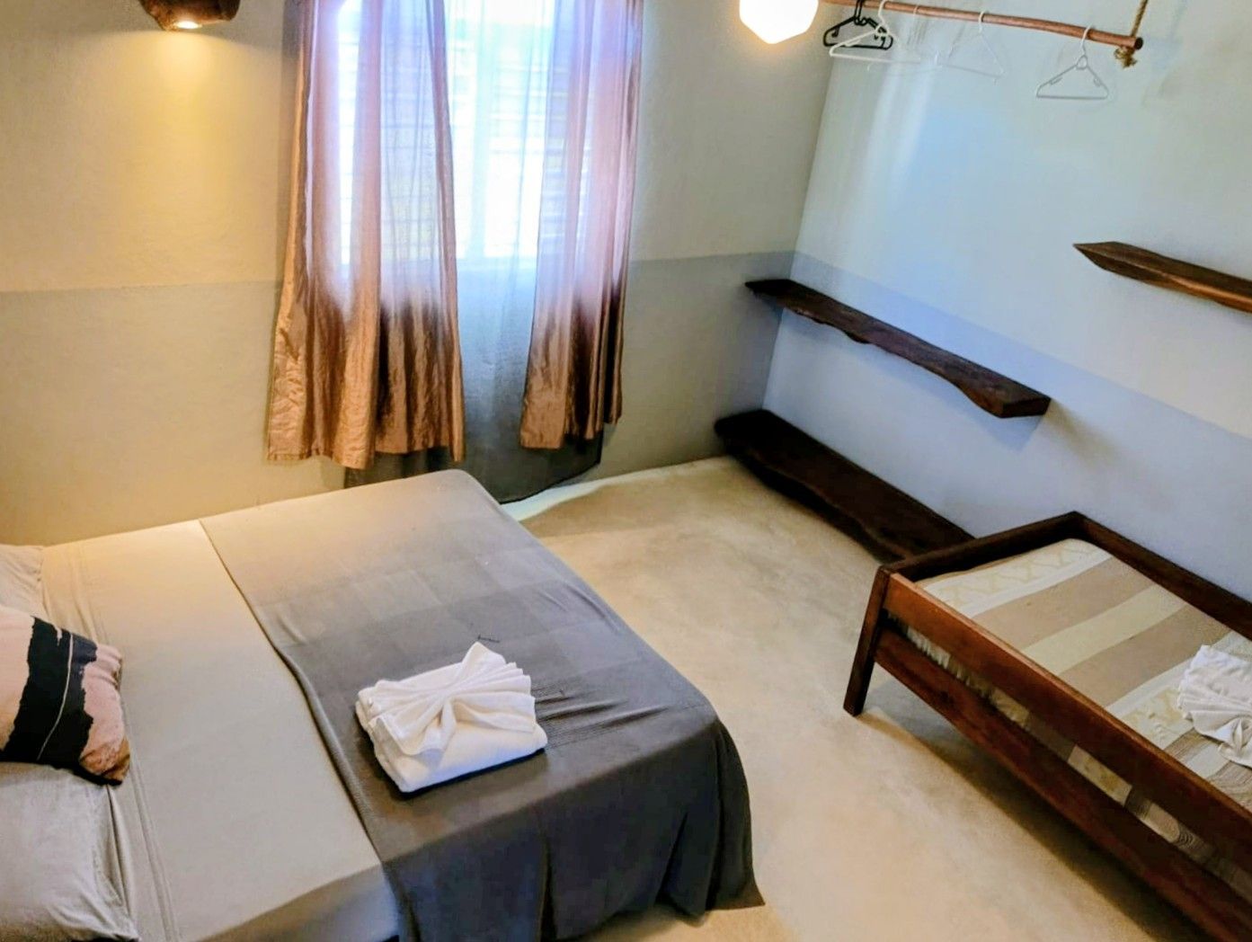 Bedroom with a large bed, small bed, curtains, and wooden shelves.