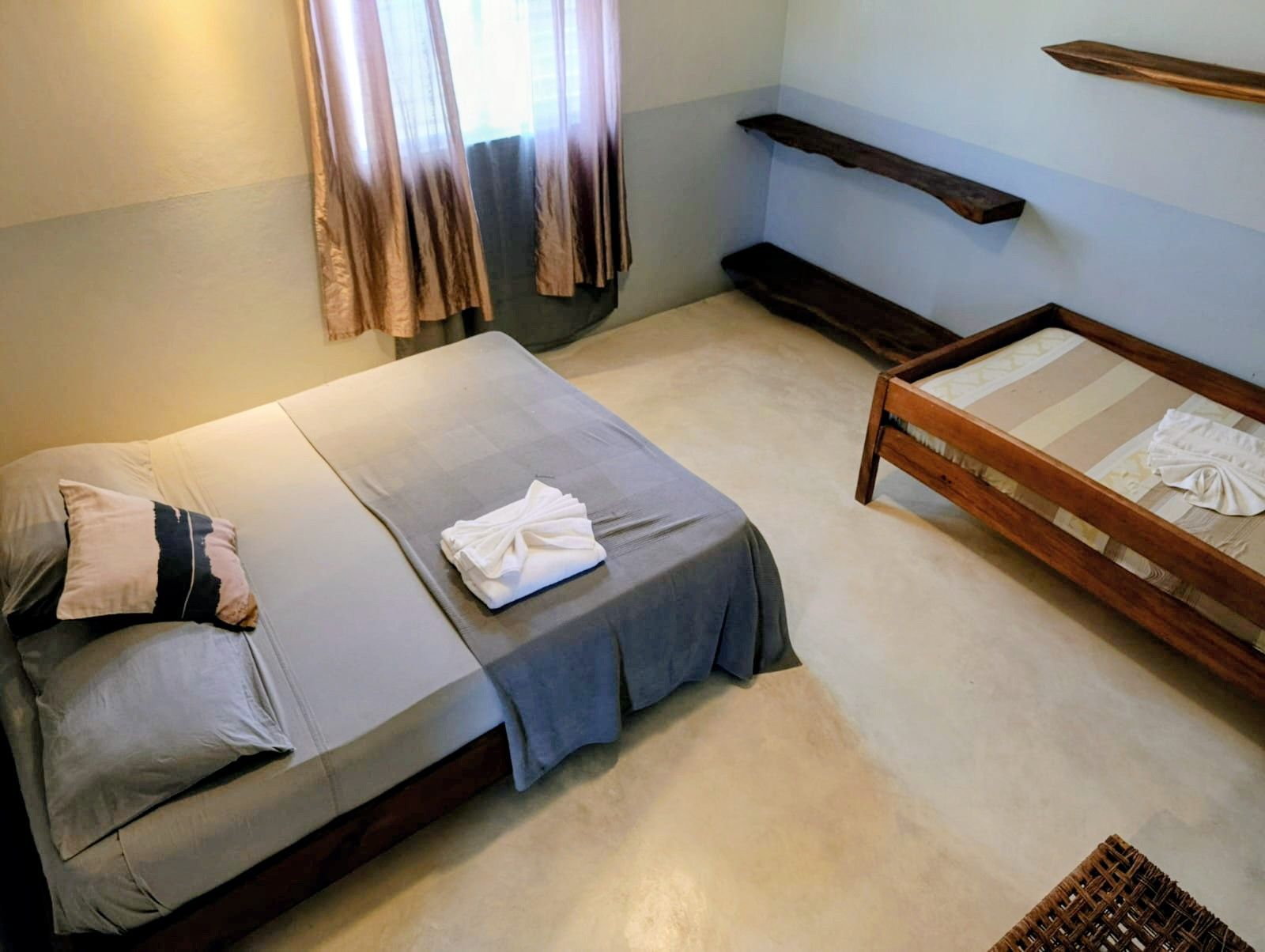 Bedroom with two beds, gray bedding, wooden frames, light walls, natural light from window.