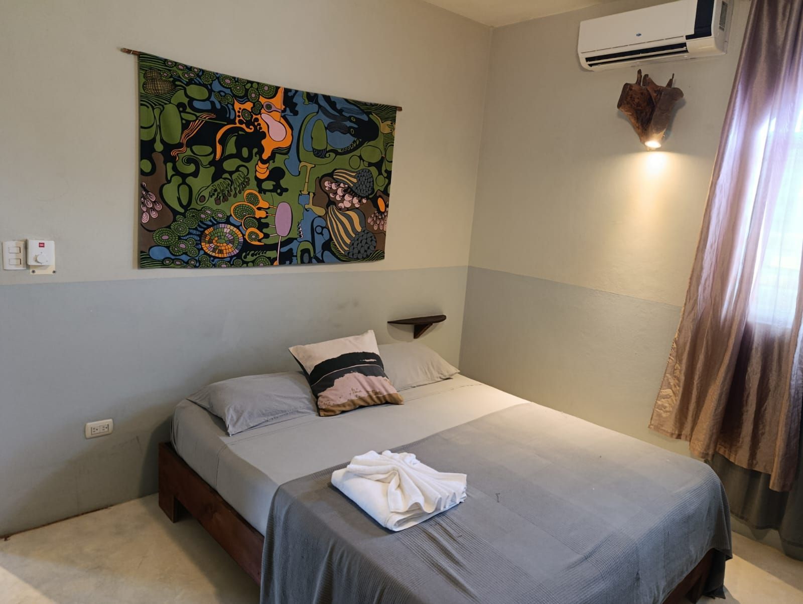 Bedroom with gray bedding, a colorful tapestry, and a window with curtains.