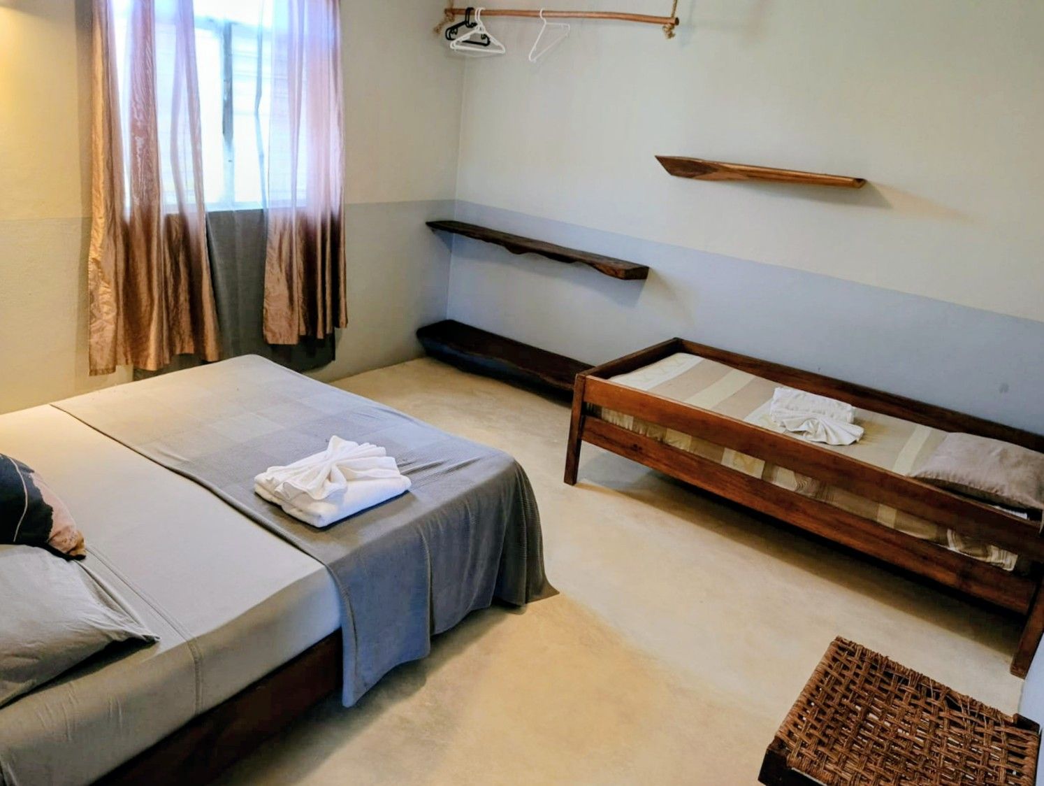Bedroom with a large bed, a single bed, wooden shelves, and curtains.