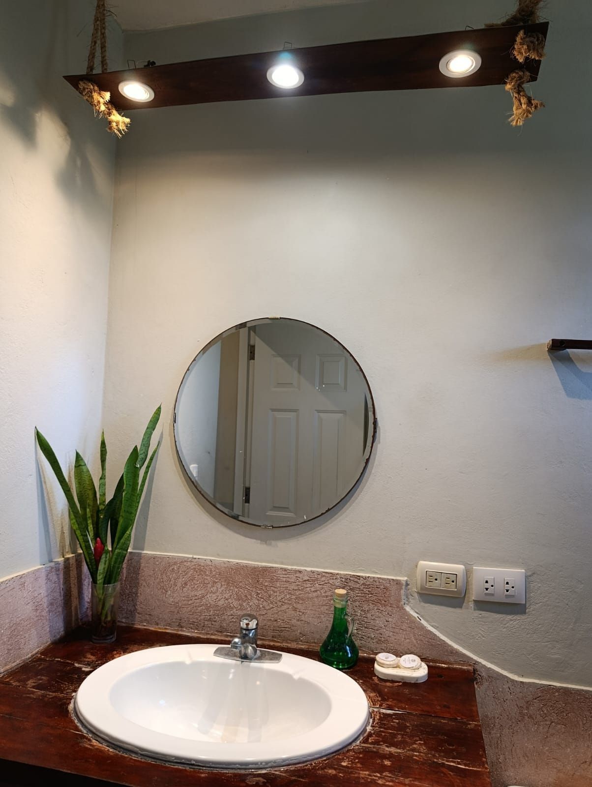 Bathroom with a round mirror above a sink; wooden counter and light fixture.