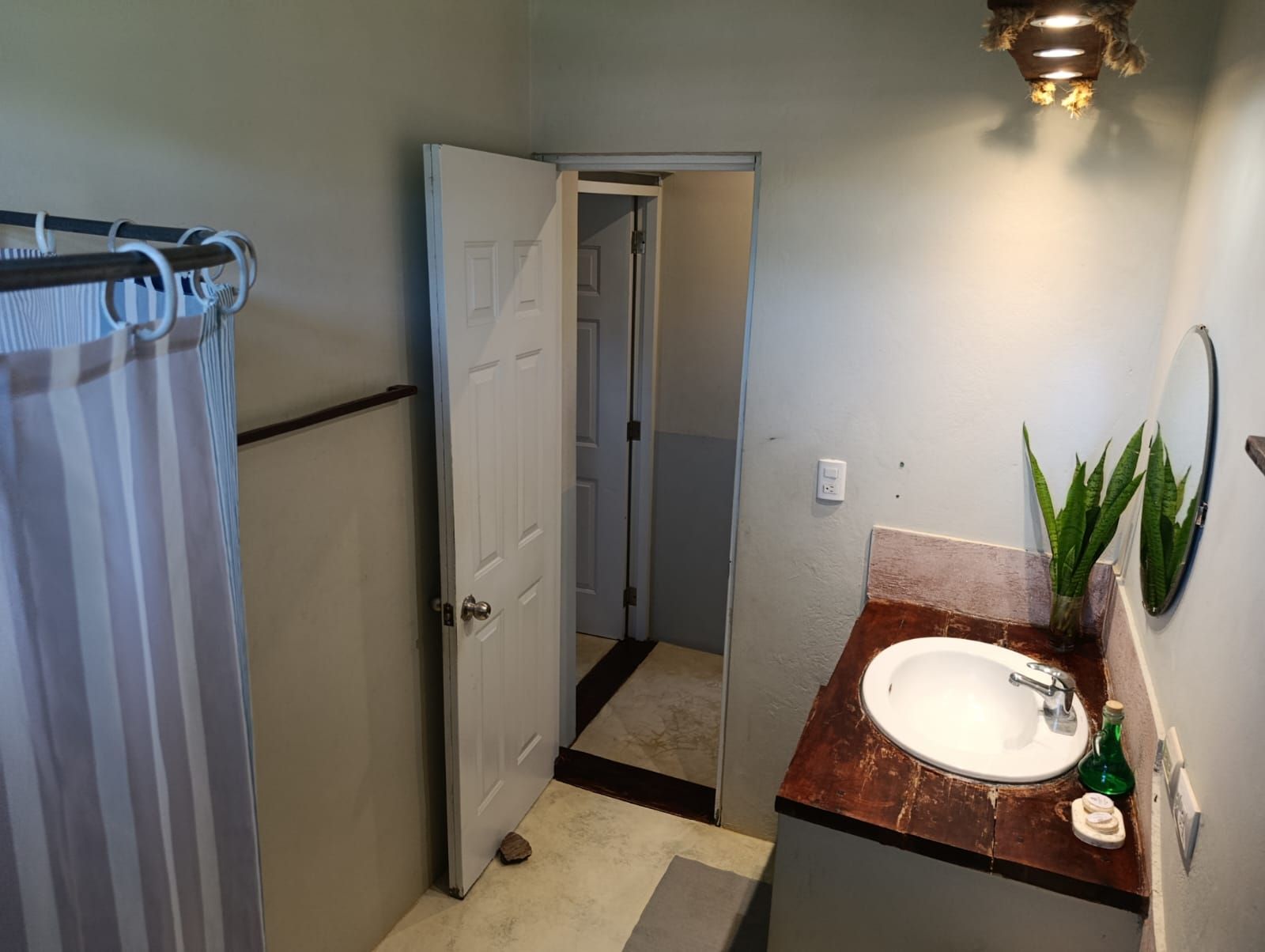 Bathroom with sink, open door to another room, and shower with curtain.