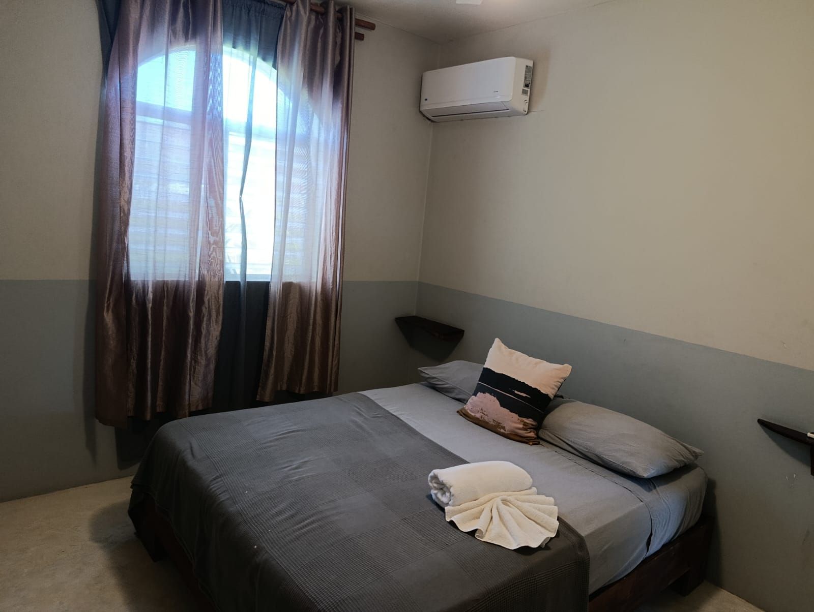 Bedroom with a bed, window with curtains, and air conditioner. Gray and beige tones.