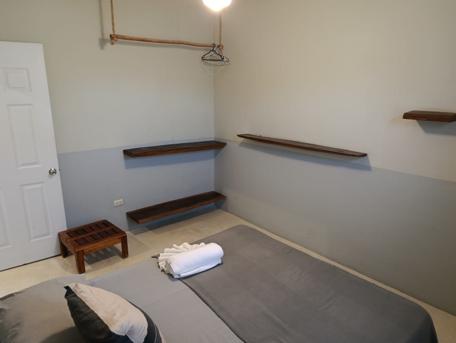 Bedroom with gray bed, wooden shelves, white door, and small wooden table.