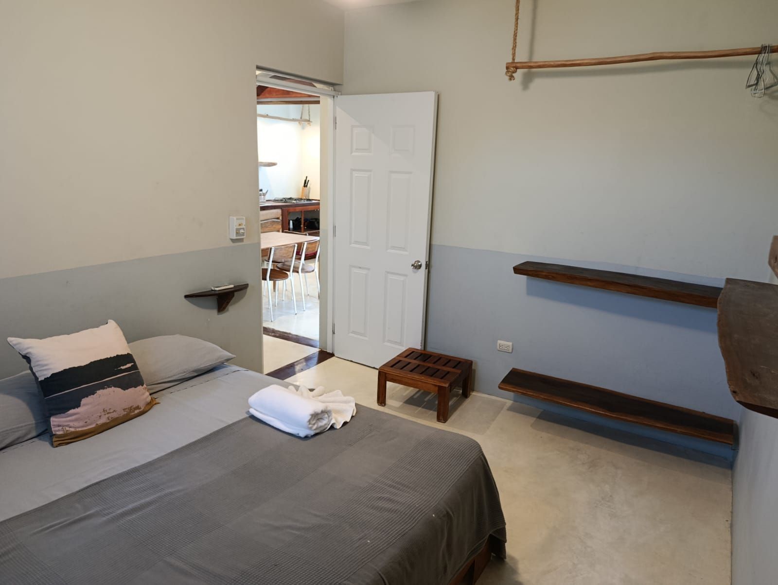 Bedroom with gray walls, bed, open door to dining area, and wooden shelves.
