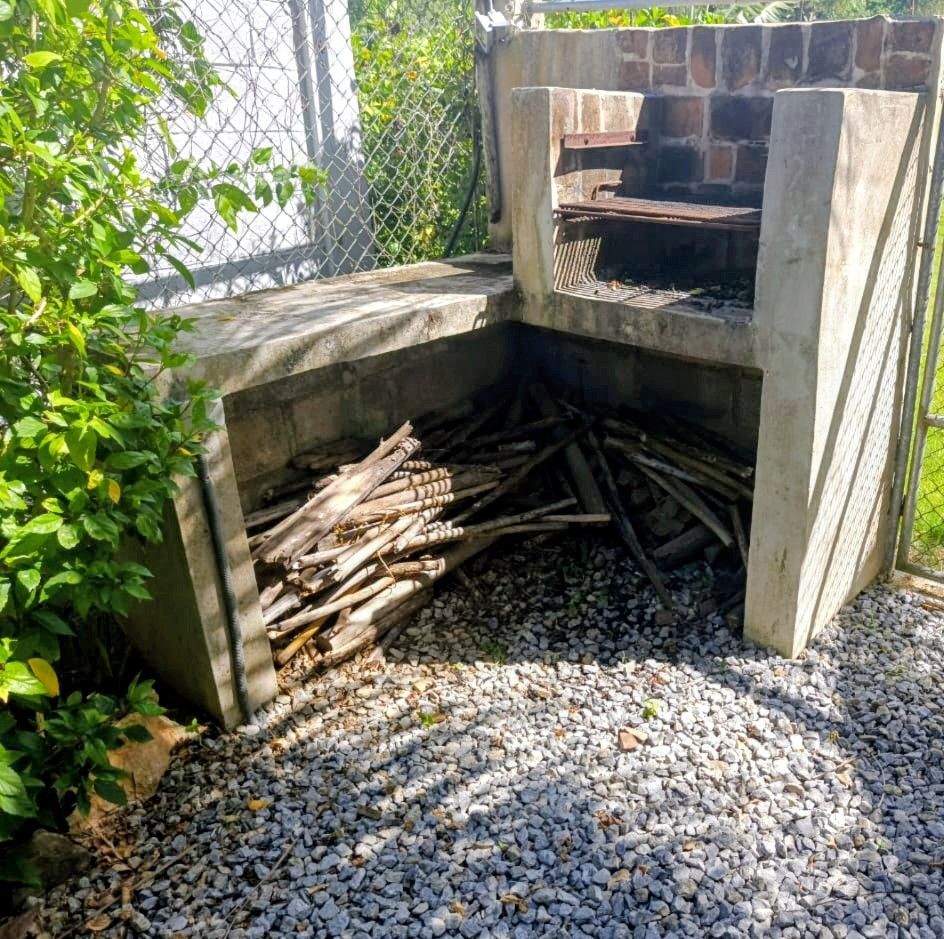 Outdoor concrete barbecue grill with wood storage, stocked with firewood, set on gravel.