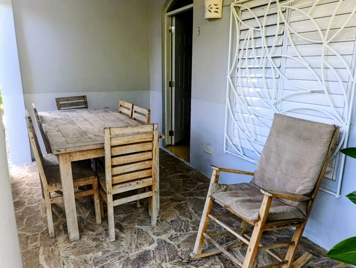 Covered patio with wooden table and chairs, and a rocking chair.