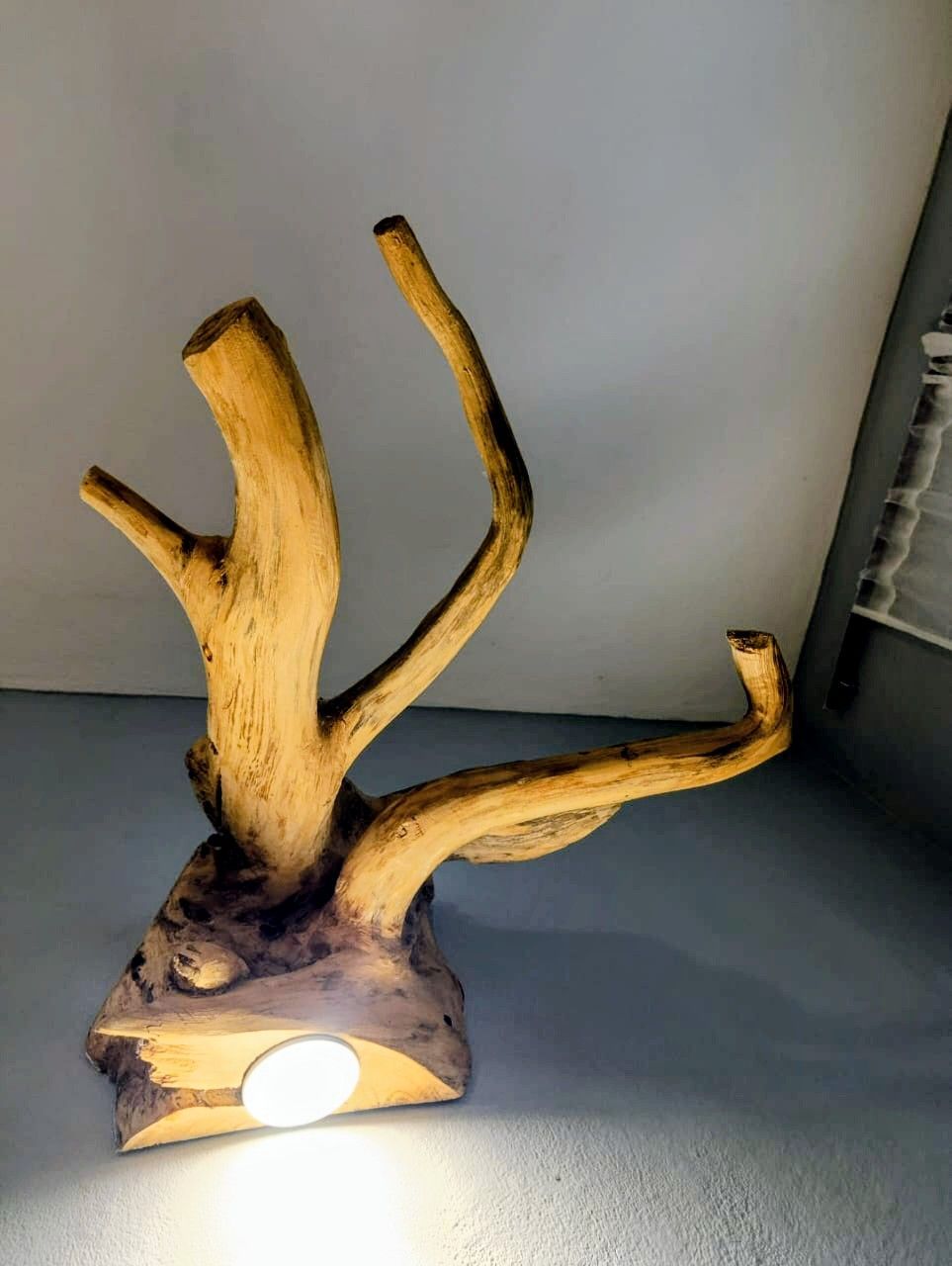 Wooden lamp shaped like a tree with a bright light on a gray wall.