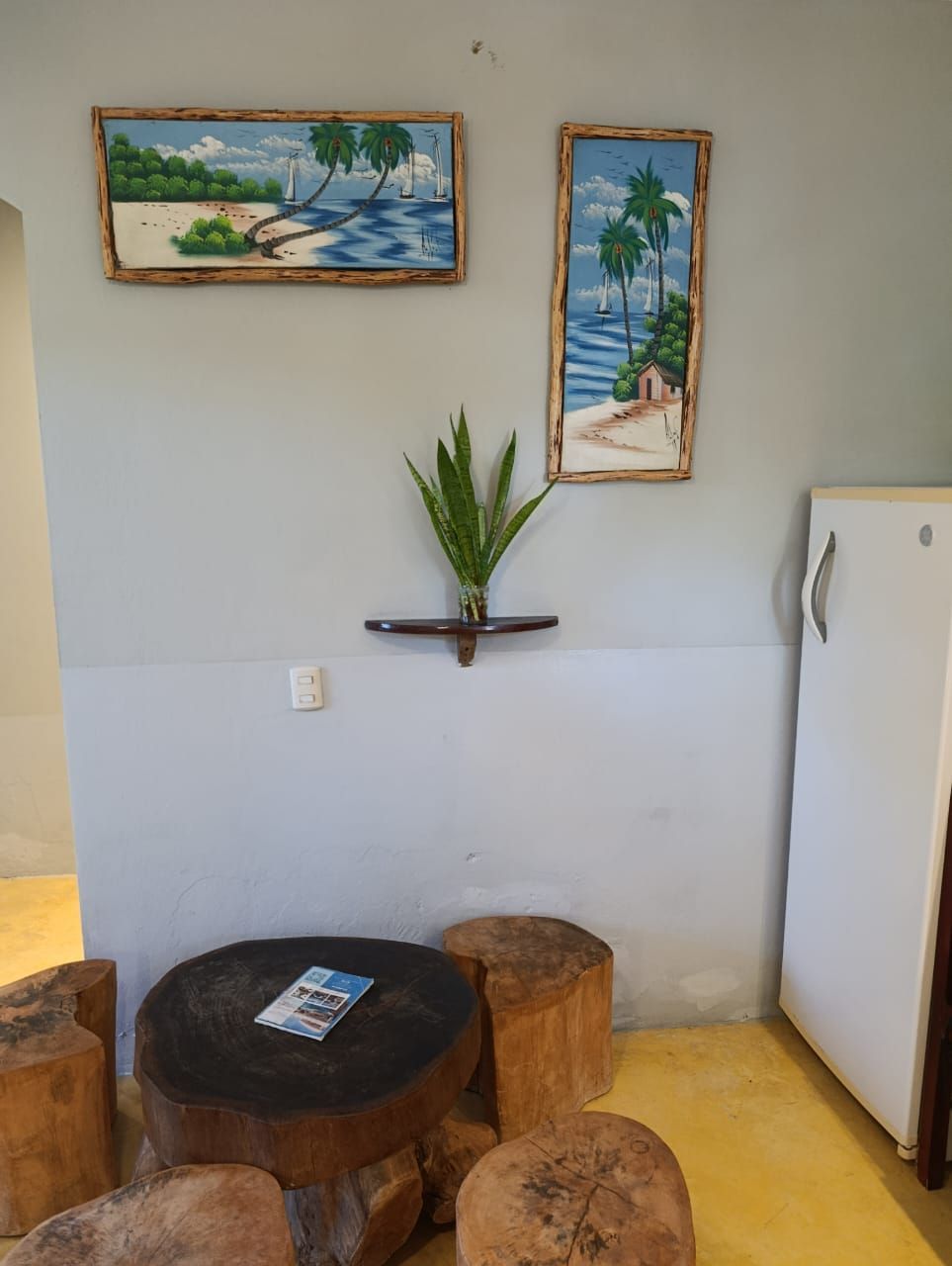 Coastal-themed artwork on light blue wall above tree stump seating. Plant on wooden shelf.