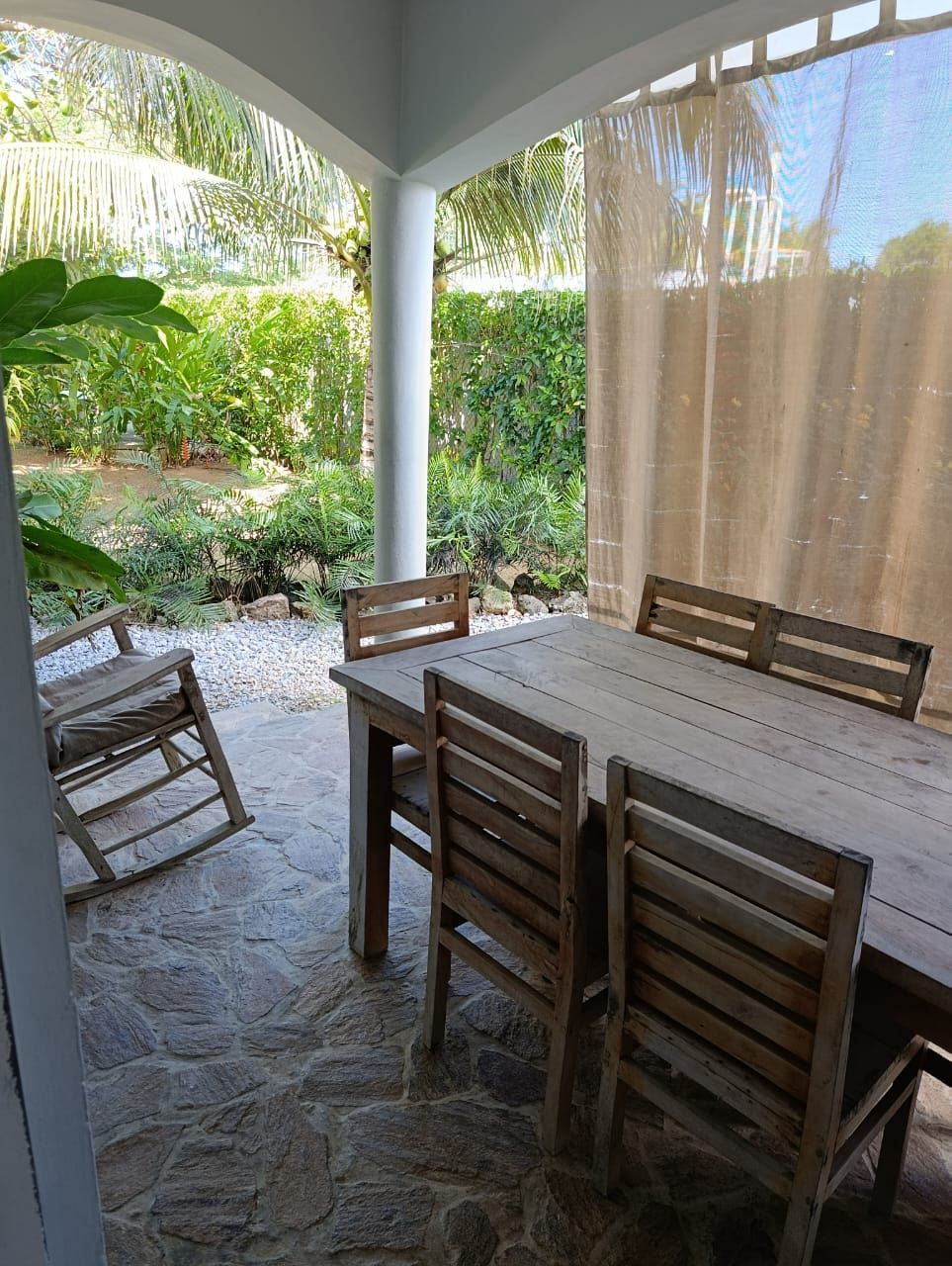 Covered patio with wooden table and chairs, stone floor, and a garden view.