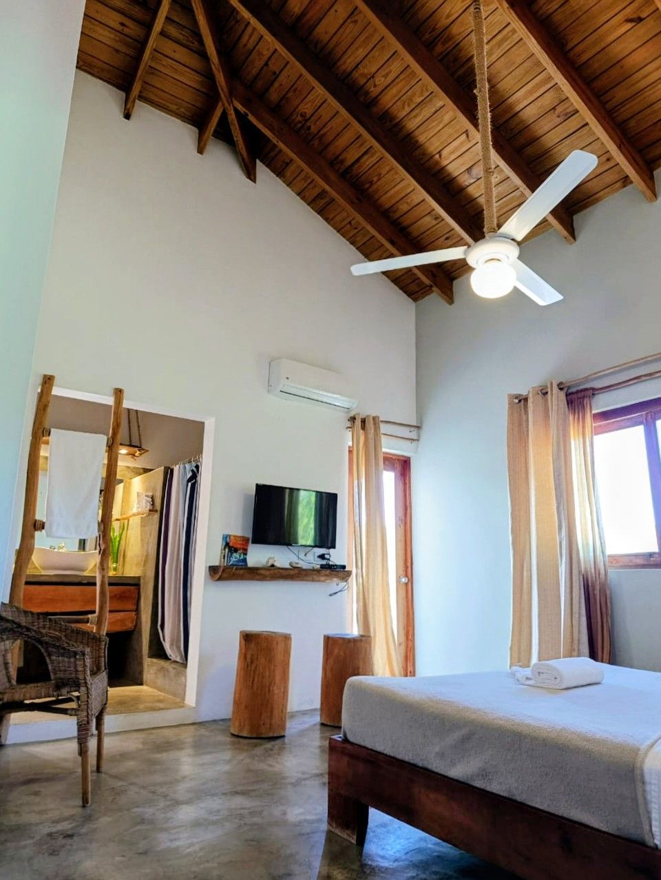 Bedroom with a bed, rustic furniture, bathroom, and a high, wooden ceiling.