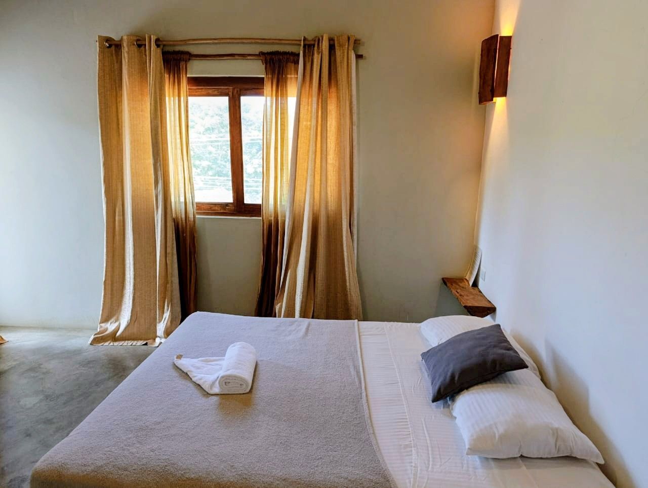 Bedroom with bed, window with gold curtains, and a wooden wall sconce.
