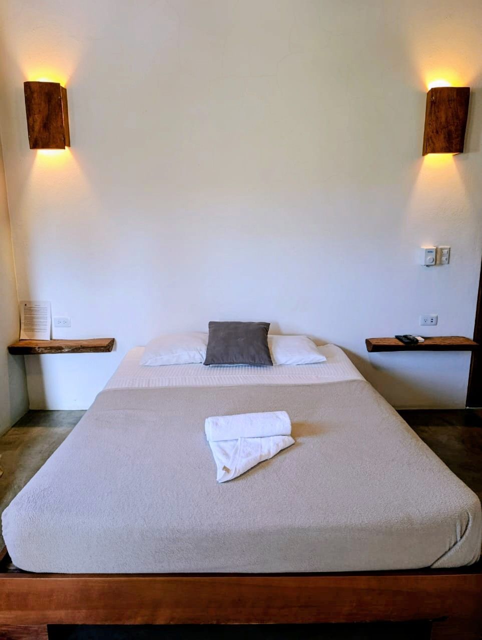 Bedroom with bed, white walls, wooden sconces, and floating bedside shelves.