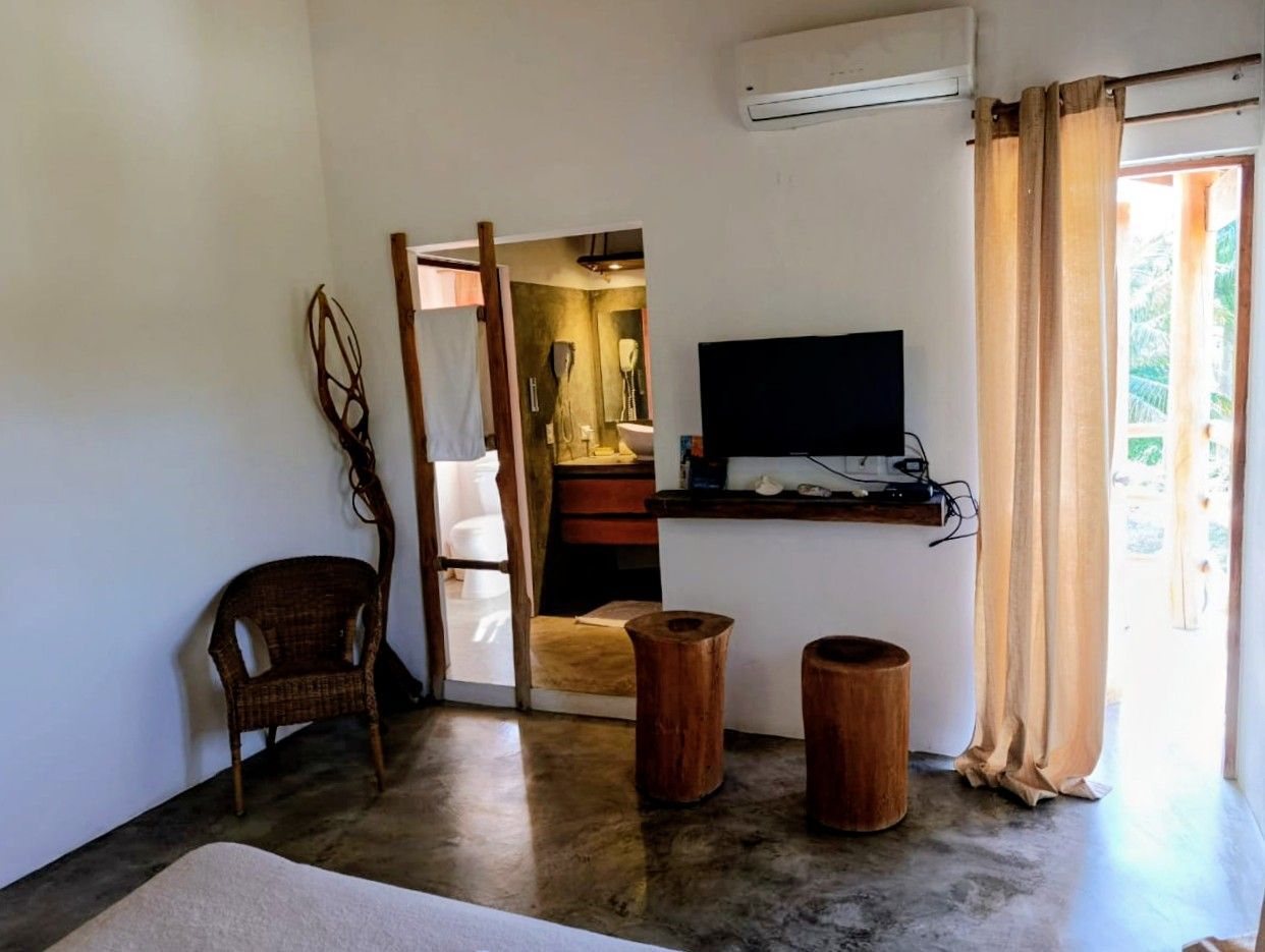 Room interior with concrete floor, open doorway to a bathroom, TV, chair, and two wooden stools.
