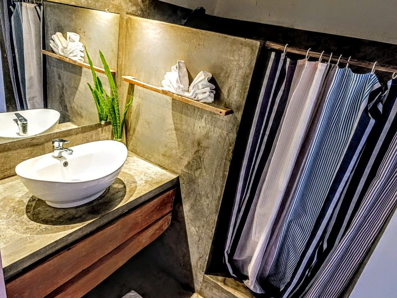 Bathroom with concrete walls, oval sink, wooden counter, and striped shower curtain.