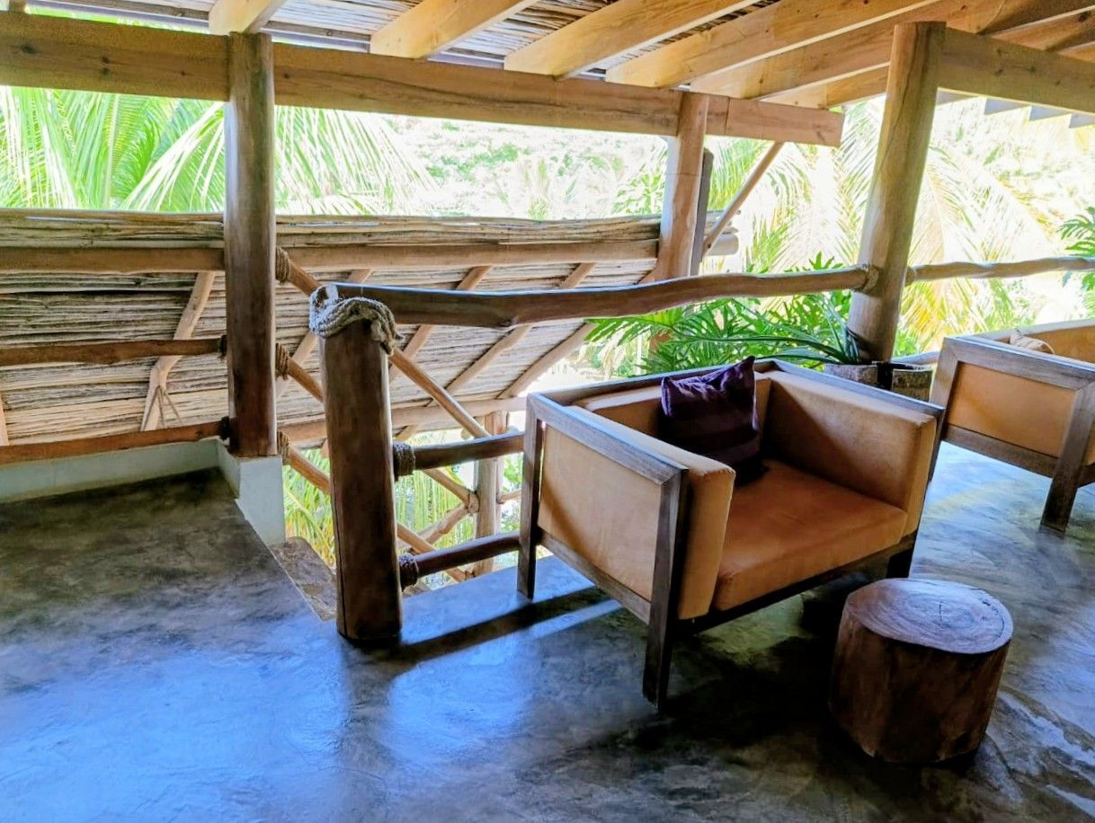 Rustic outdoor seating area with wood beams, concrete floor, and two armchairs with a tree stump table.