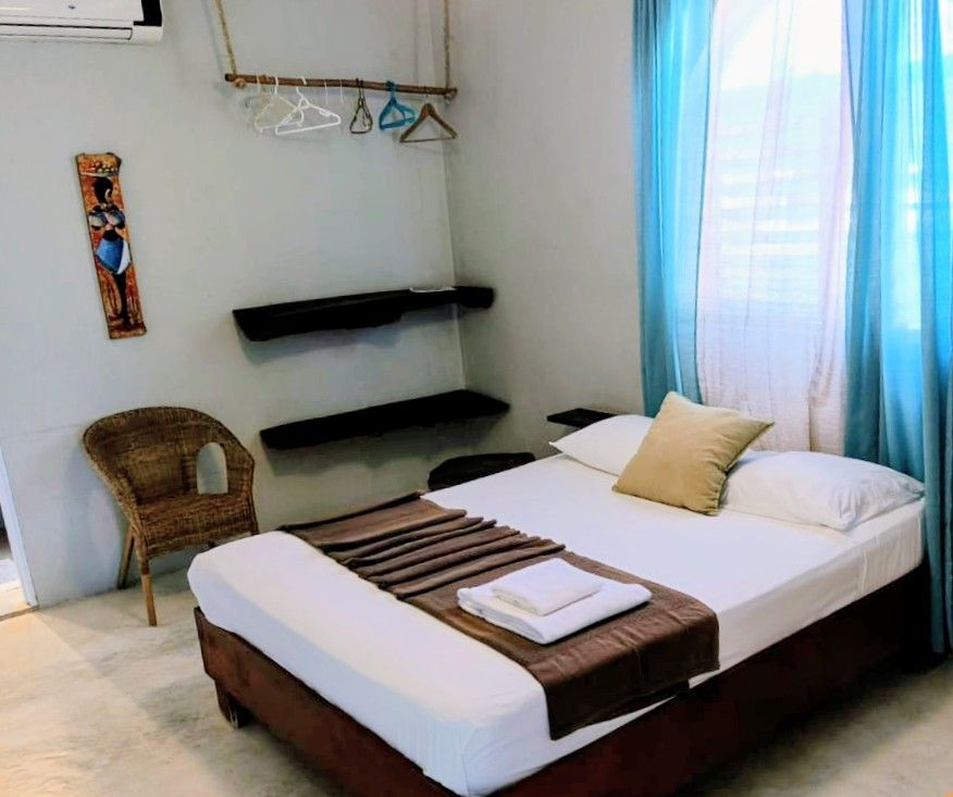 Bedroom with bed, wicker chair, shelves, and blue curtains.