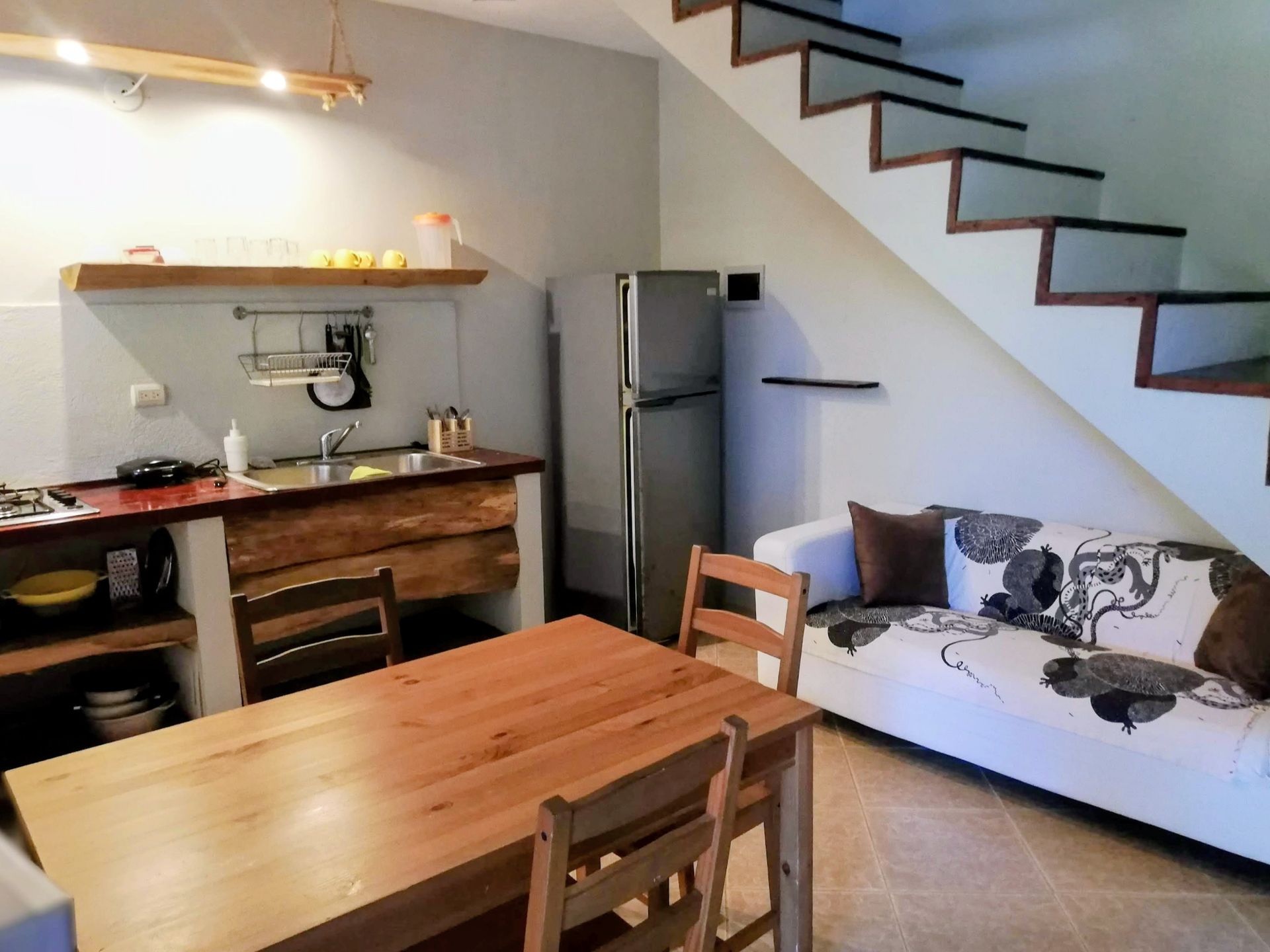 Small kitchen and dining area with a sofa, stairs, and fridge. Wooden table and counter.