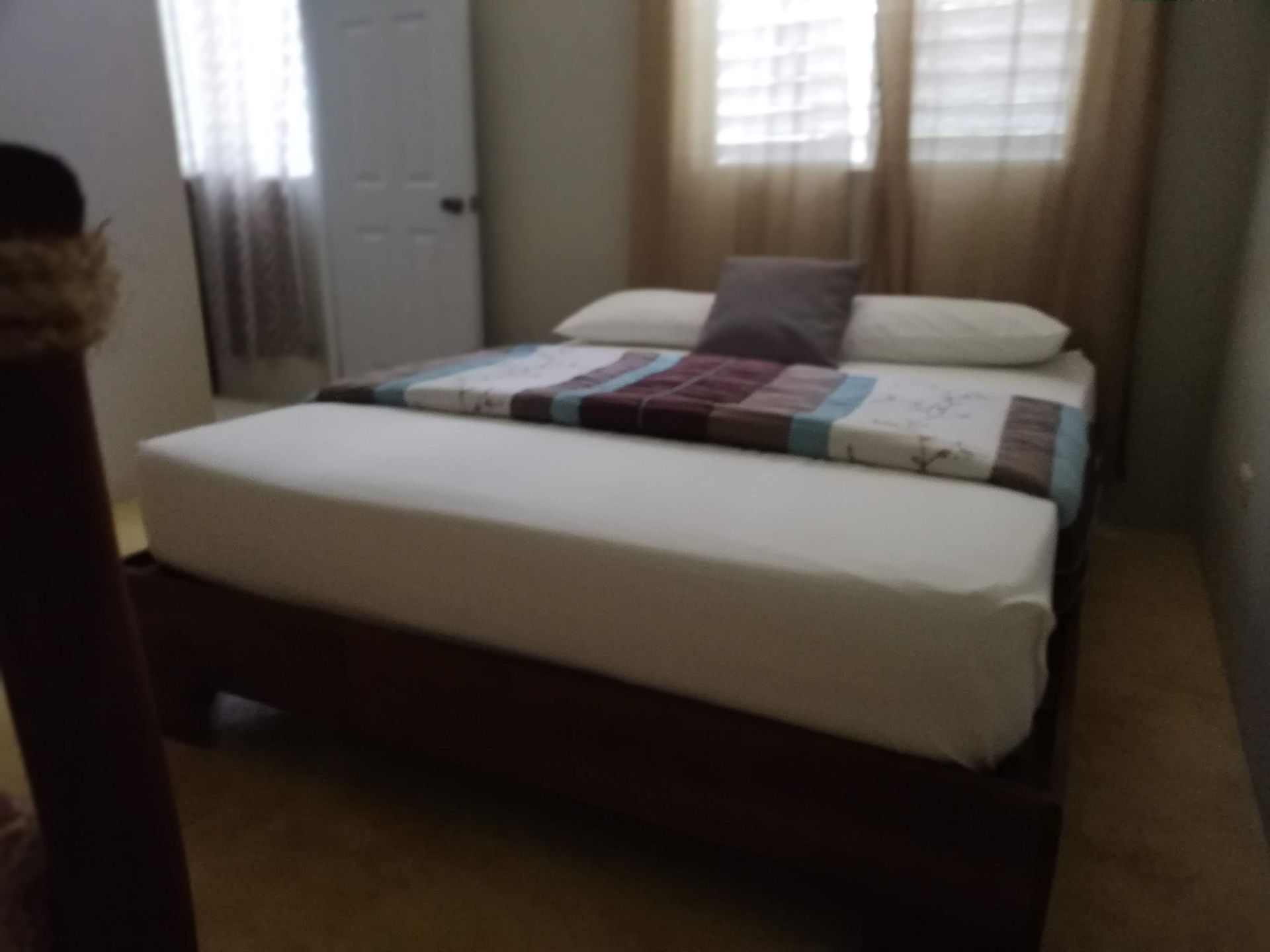 Bedroom with a large bed, white sheets, and patterned blanket. A door and windows are visible.