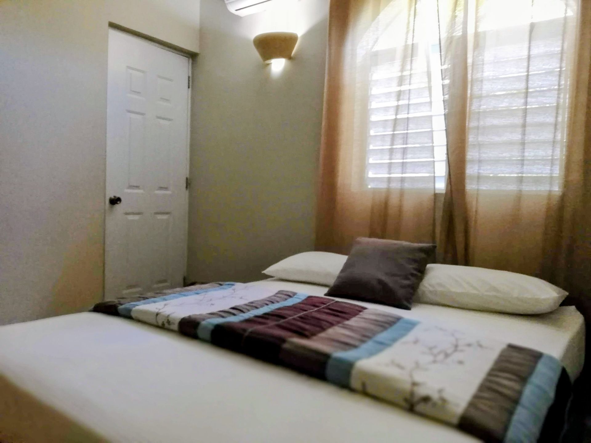 Bedroom with a bed, white door, windows with blinds, and brown curtains.