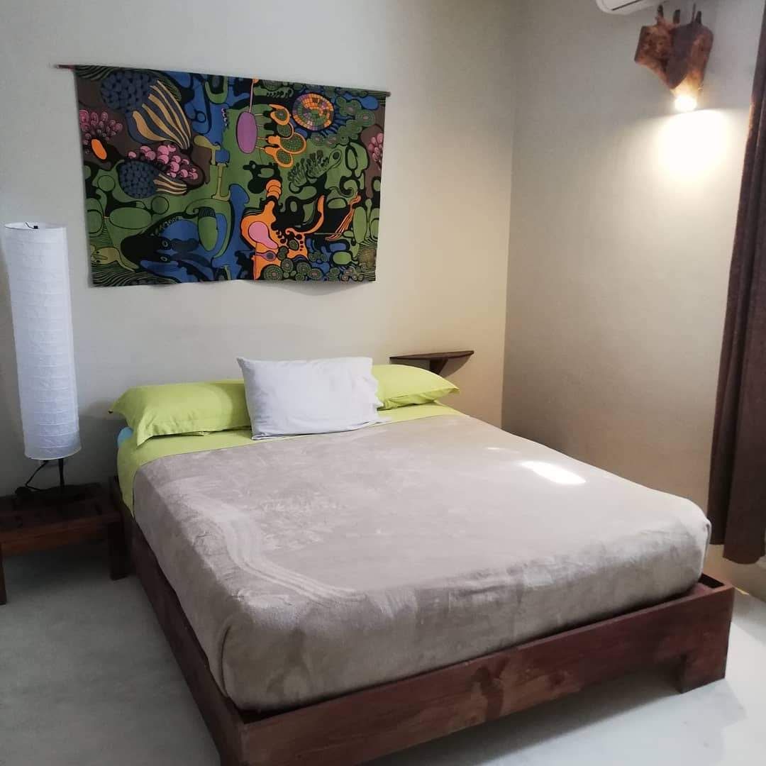 Bedroom with wooden bed, colorful tapestry, and a tall lamp.