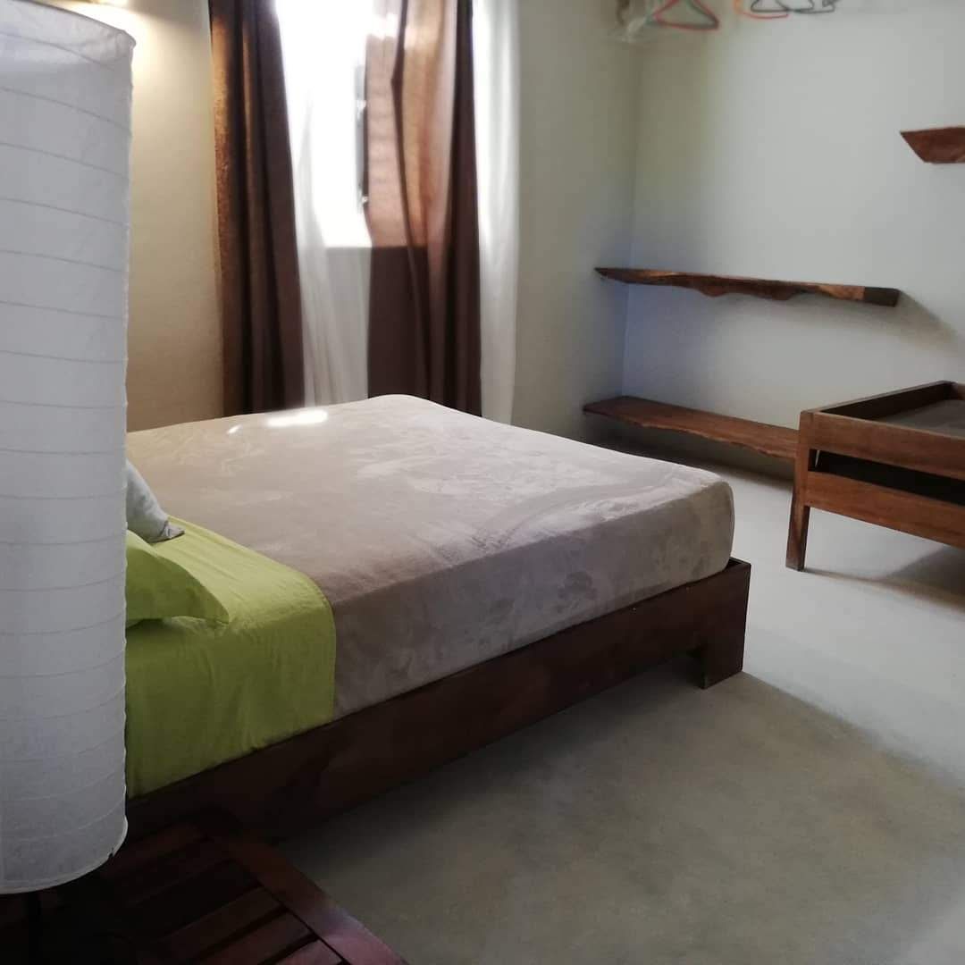 Bedroom with bed, shelves, and window with brown curtains. Green, brown and beige tones.