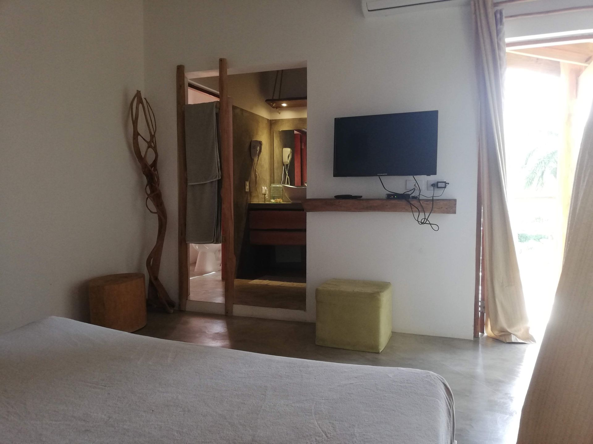 Bedroom with bed, TV, bathroom doorway, and open curtain to outside.