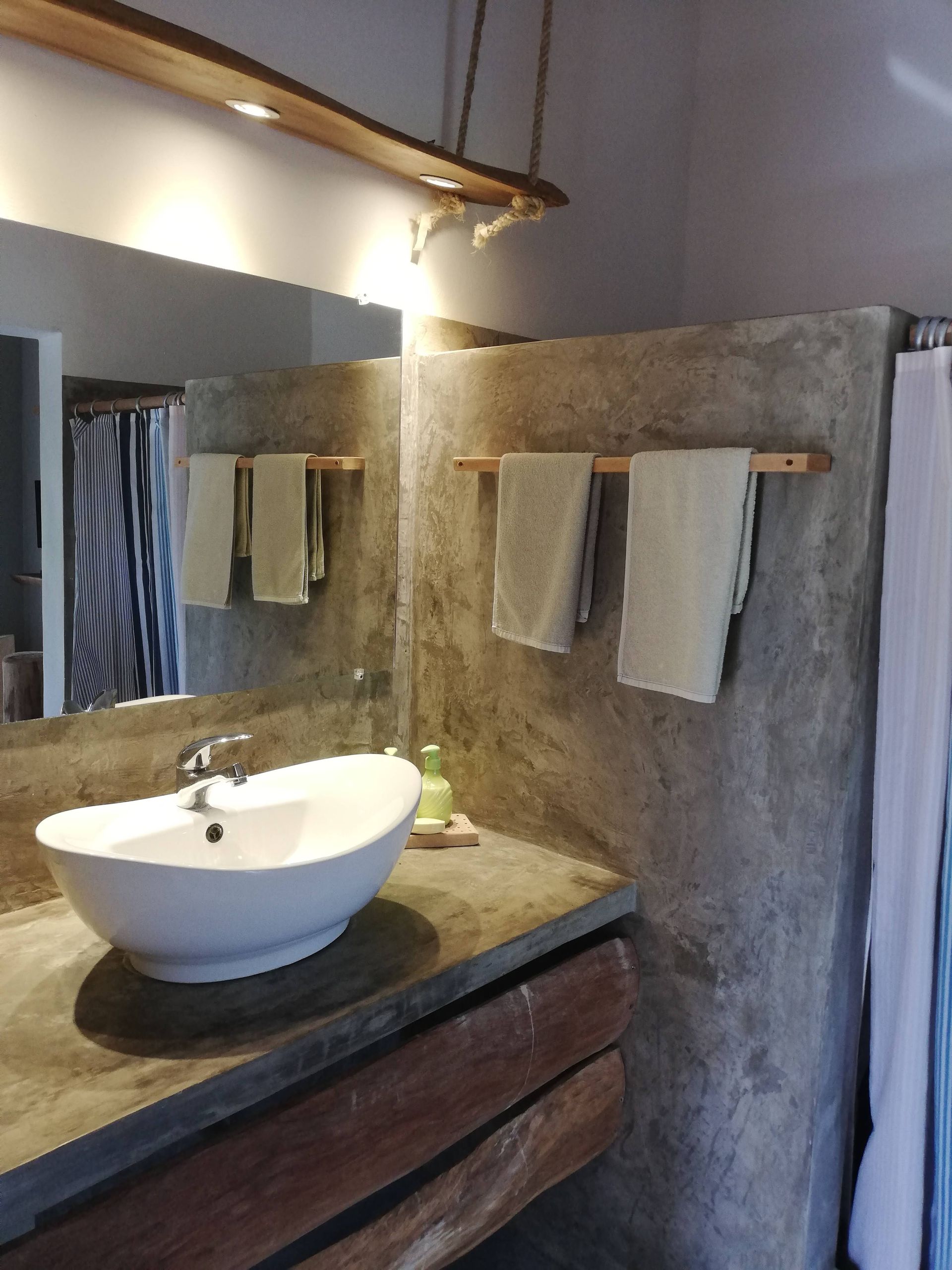 Bathroom with a white sink, concrete countertop, and towels on a wooden rack against a gray wall.