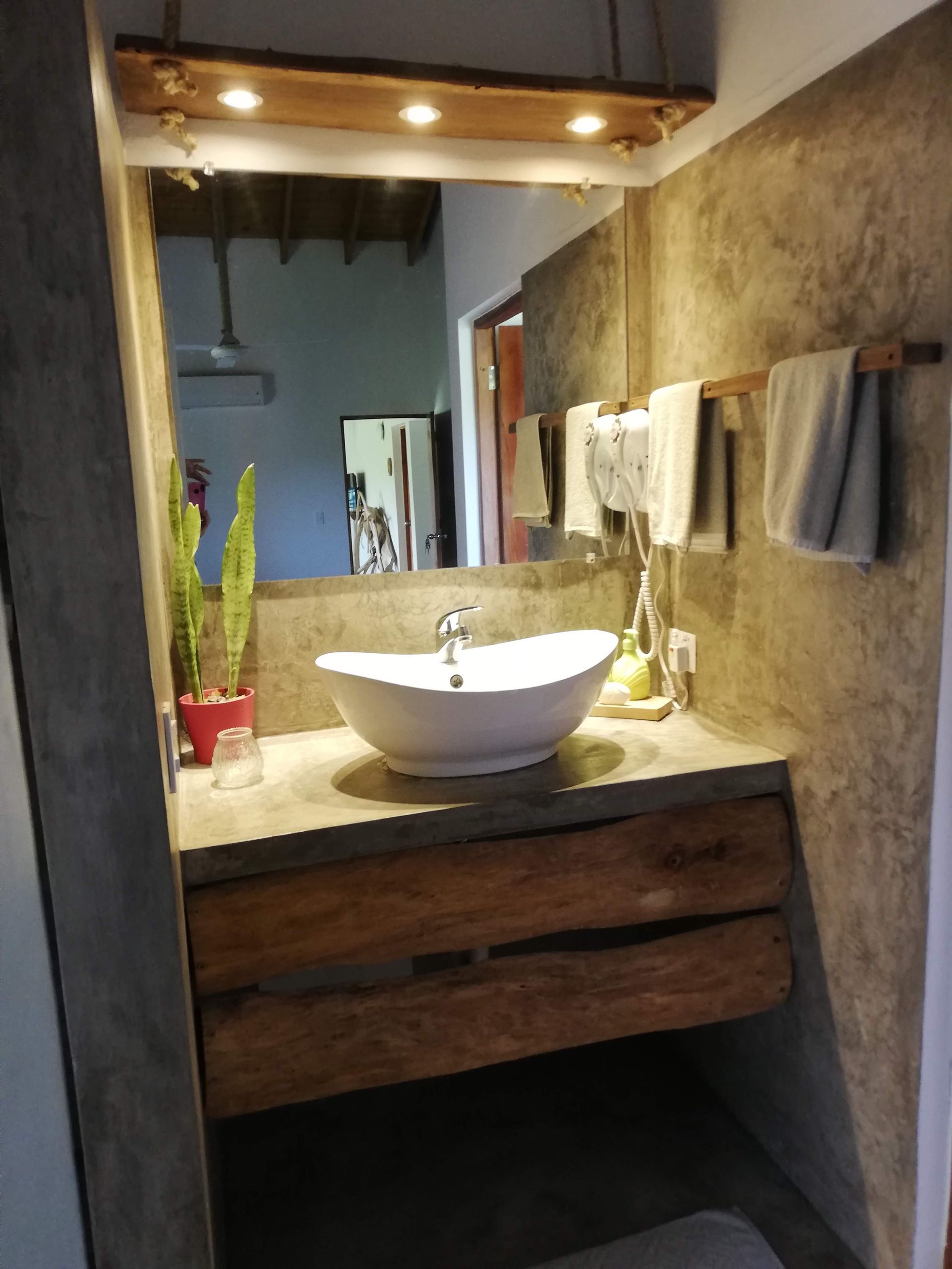 Bathroom with a white oval sink, wooden drawers, concrete walls, and a large mirror.