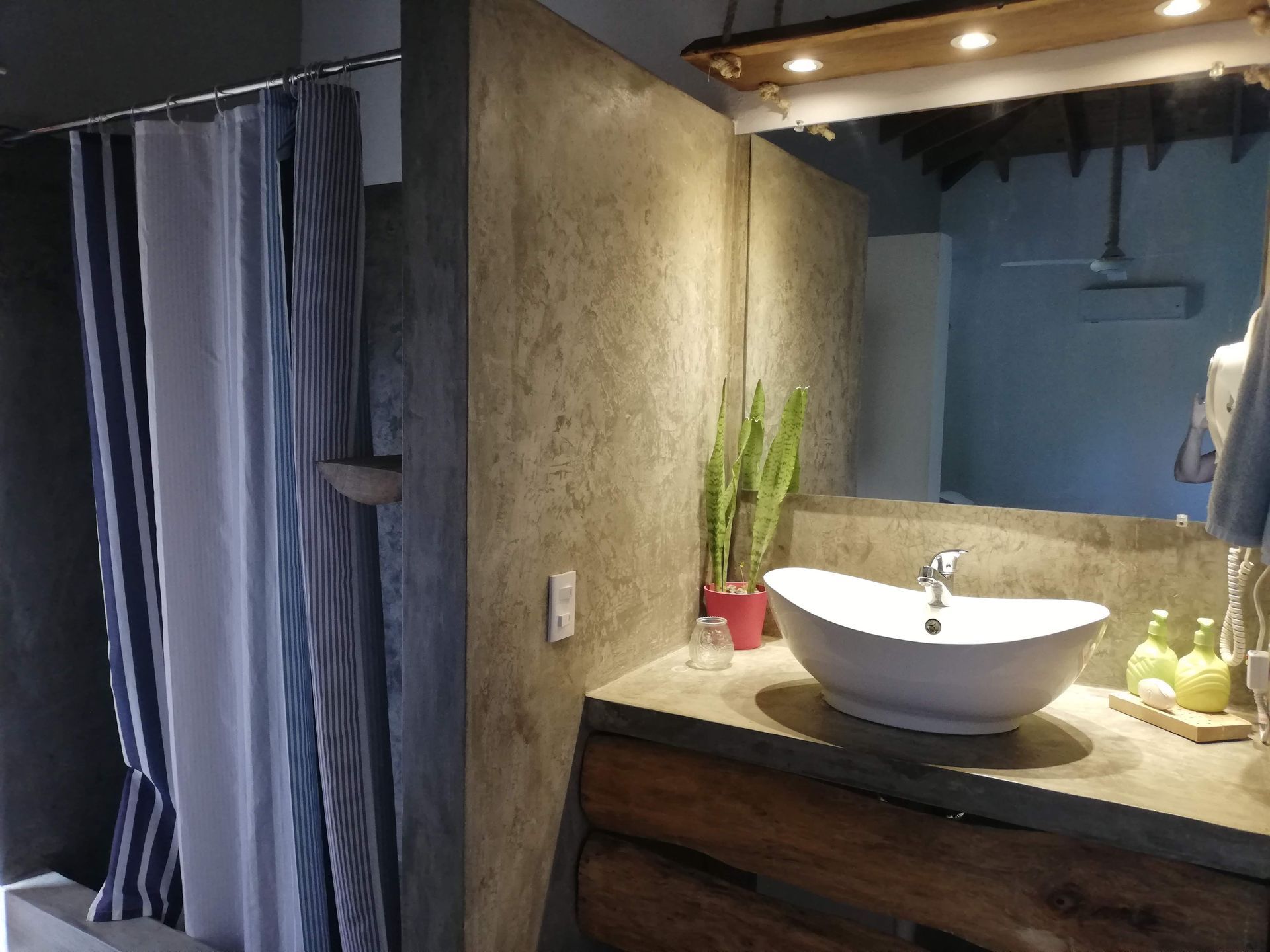 Bathroom with sink, mirror, shower, and concrete walls. Features a rustic wooden cabinet.